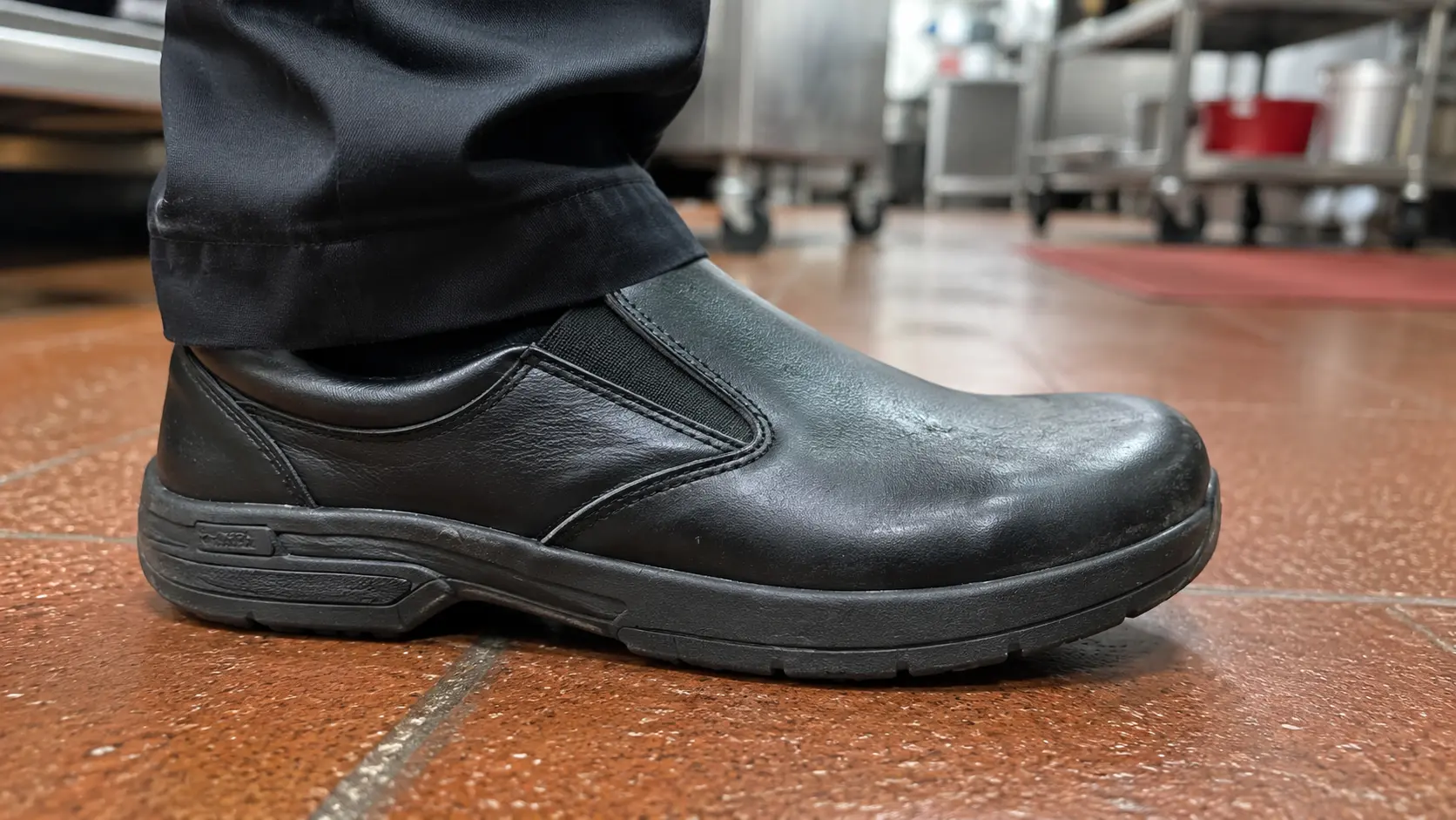 Plain dark slip-on work shoe on a commercial kitchen tile floor.